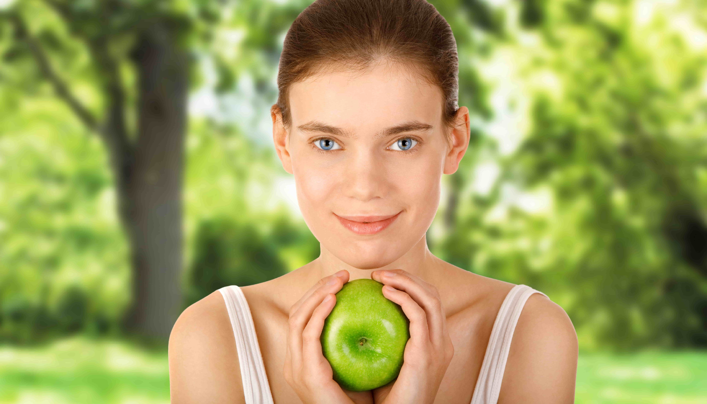 A woman holding an apple in front of her face, showcasing a healthy lifestyle choice.